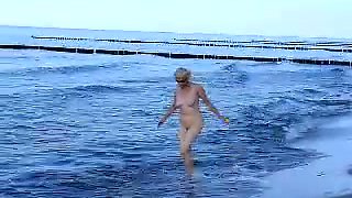 Naked old woman playing and having fun on the beach